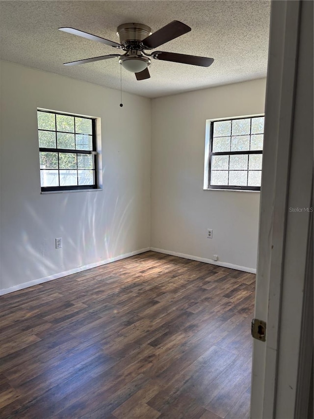 empty room featuring a textured ceiling, baseboards, and dark wood-type flooring