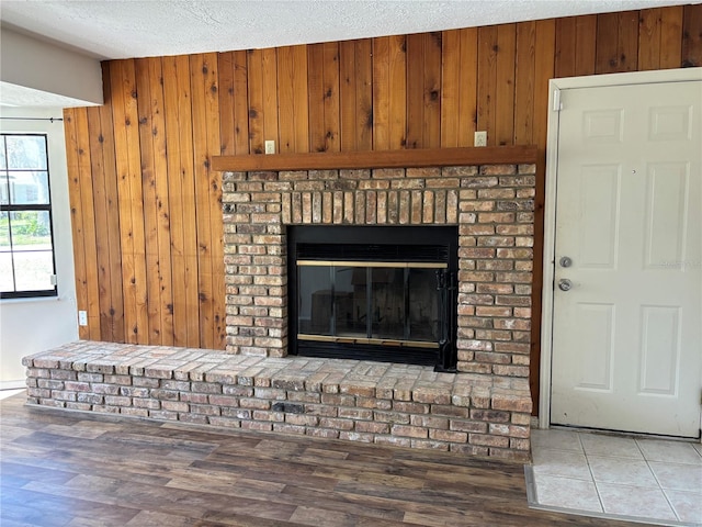 interior details featuring a brick fireplace, wooden walls, a textured ceiling, and wood finished floors