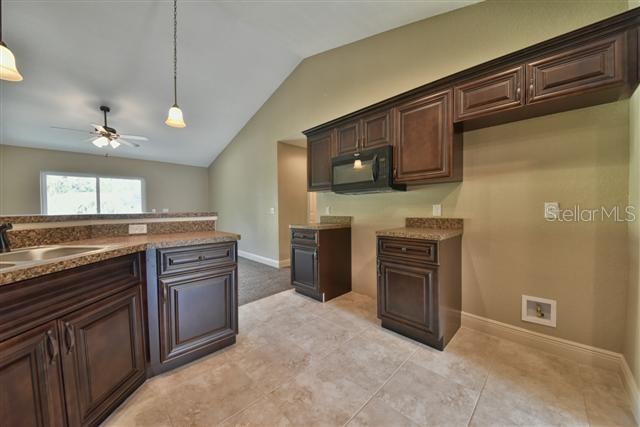 kitchen with dark brown cabinetry, decorative light fixtures, vaulted ceiling, black microwave, and a sink