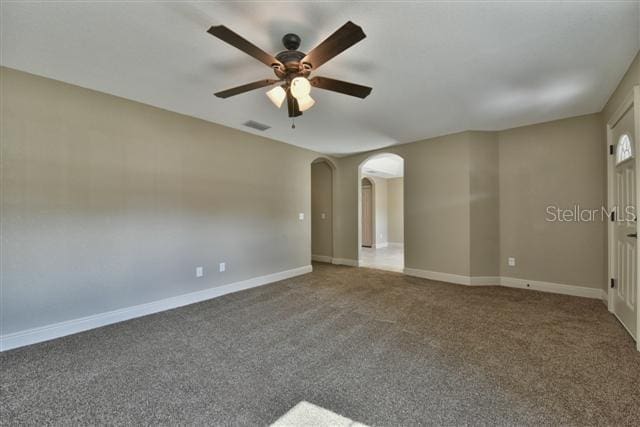 empty room featuring visible vents, arched walkways, baseboards, ceiling fan, and carpet