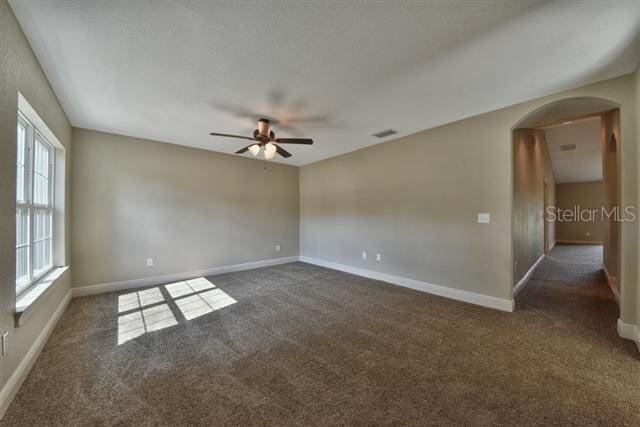 unfurnished room featuring carpet, arched walkways, visible vents, ceiling fan, and baseboards