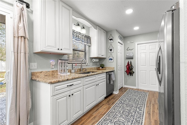 kitchen featuring stainless steel appliances, light wood-style flooring, white cabinetry, a sink, and a textured ceiling