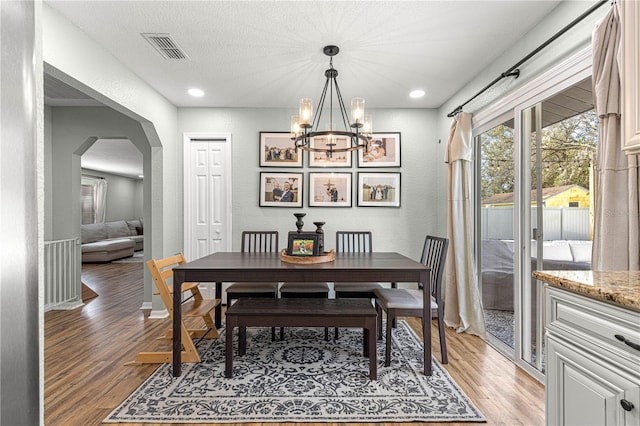 dining space with arched walkways, visible vents, a textured wall, and light wood-style flooring