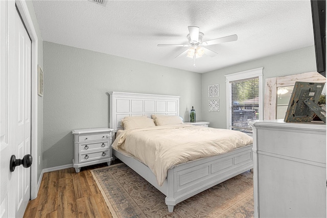 bedroom featuring a textured ceiling, a textured wall, a ceiling fan, baseboards, and dark wood-style floors