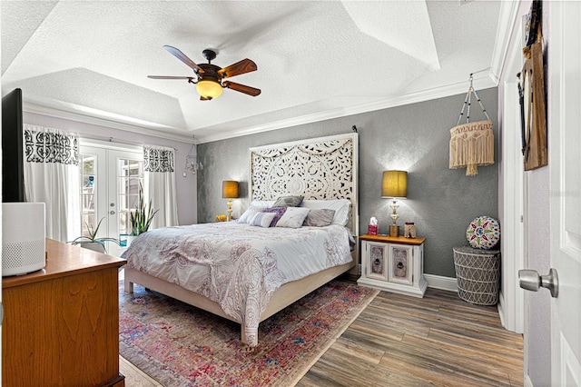 bedroom with ornamental molding, a textured ceiling, wood finished floors, french doors, and a textured wall