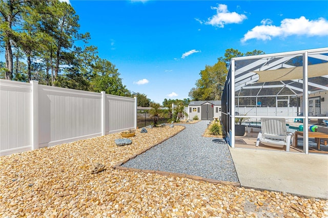 view of yard with glass enclosure, a storage shed, a fenced backyard, an outbuilding, and a patio