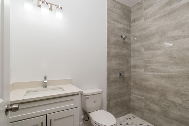 bathroom featuring a tile shower, vanity, and toilet