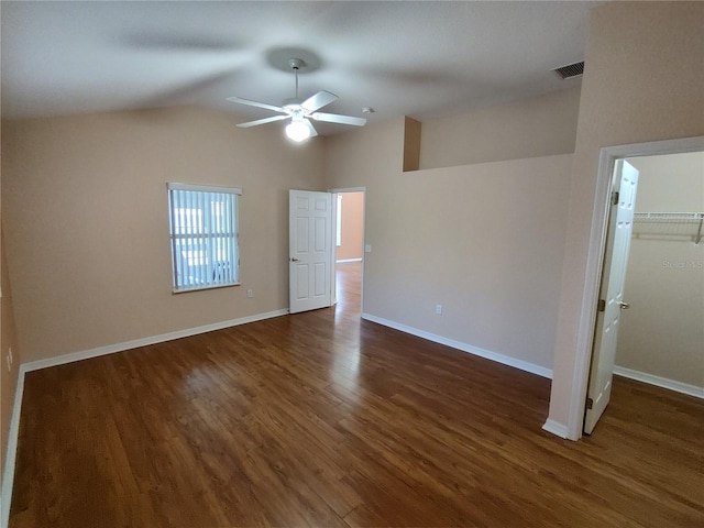 unfurnished bedroom featuring baseboards, lofted ceiling, dark wood-type flooring, a spacious closet, and a closet