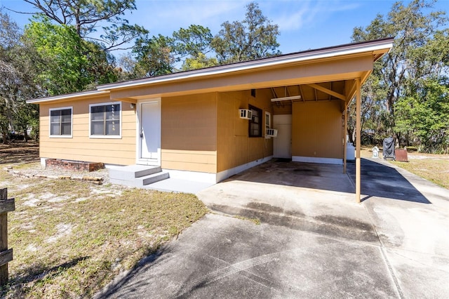 view of front of house featuring entry steps, concrete driveway, a wall mounted air conditioner, cooling unit, and a carport