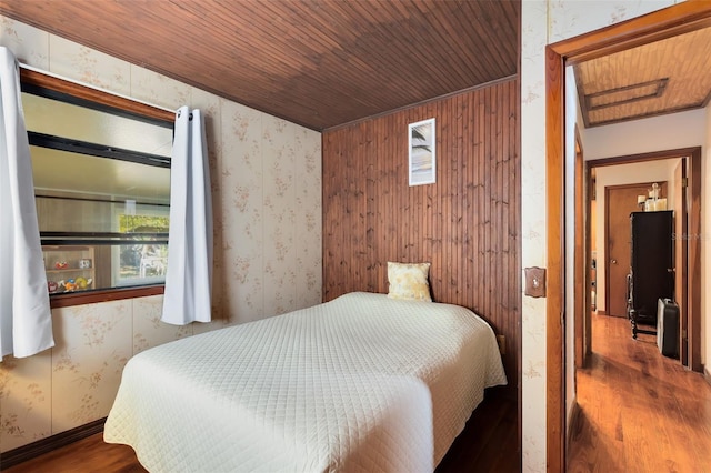 bedroom featuring wood ceiling, wood finished floors, and wallpapered walls