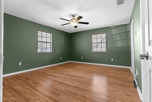 spare room with a ceiling fan, plenty of natural light, wood finished floors, and visible vents