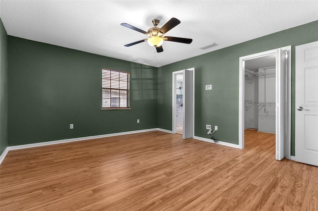 unfurnished bedroom with a spacious closet, visible vents, light wood-style flooring, and baseboards