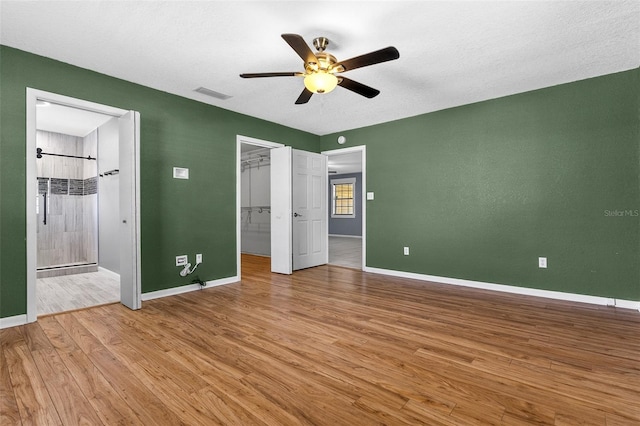 unfurnished bedroom featuring visible vents, a walk in closet, baseboards, and wood finished floors