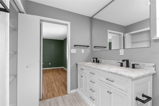 full bathroom featuring double vanity, wood finished floors, baseboards, and a sink