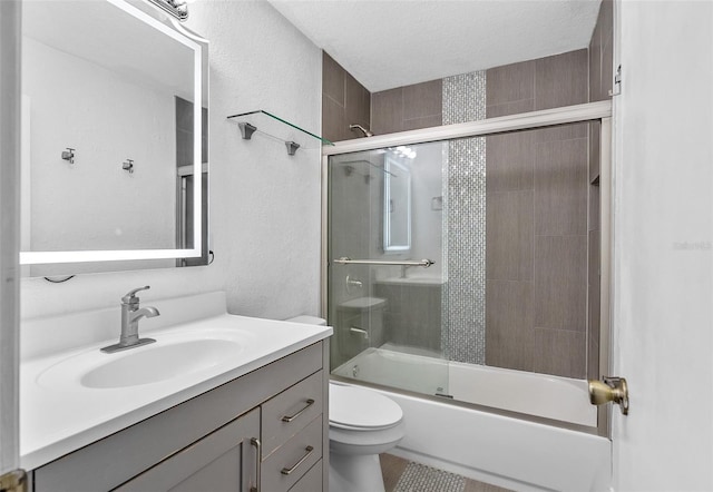 full bathroom featuring a textured ceiling, shower / bath combination with glass door, vanity, and toilet