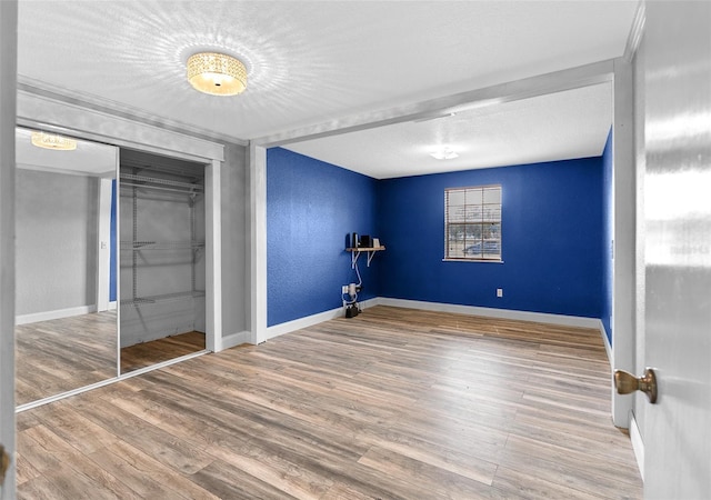 unfurnished bedroom featuring a textured ceiling, wood finished floors, a closet, baseboards, and a textured wall