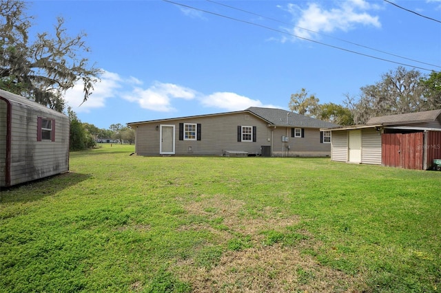 rear view of property with an outbuilding, central AC unit, a storage unit, and a yard