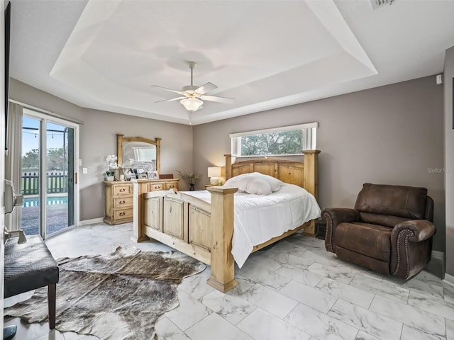 bedroom with marble finish floor, access to outside, and a raised ceiling