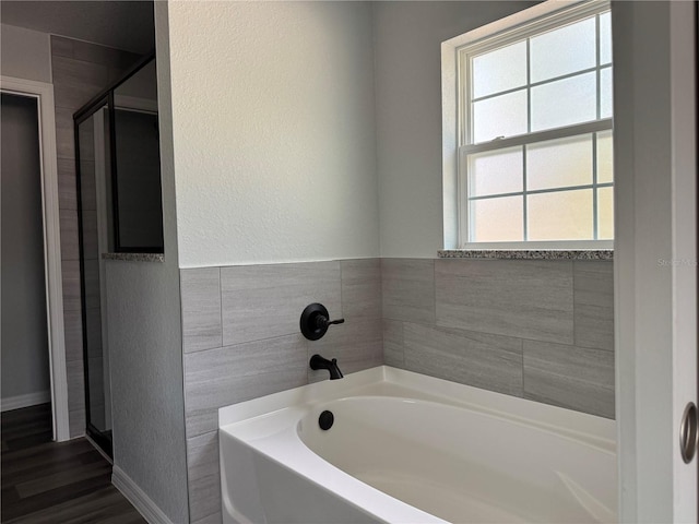 bathroom featuring a textured wall, a shower stall, a bath, and baseboards