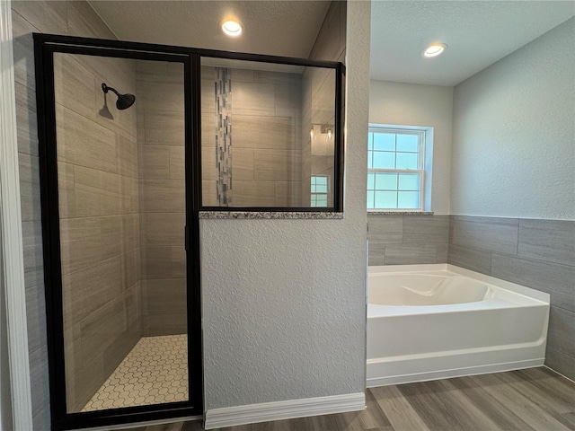 bathroom with a textured wall, wood finished floors, a textured ceiling, a shower stall, and a bath