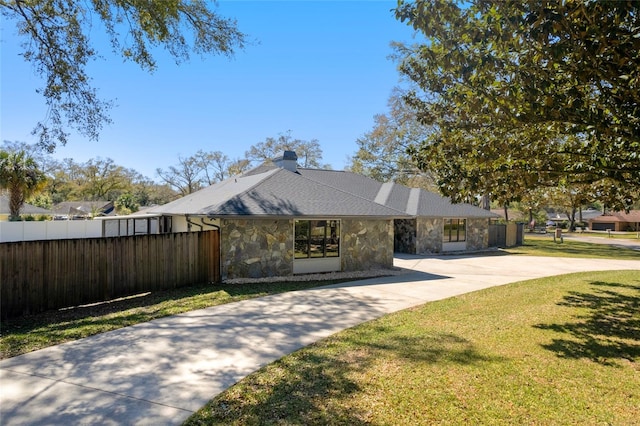 view of front facade featuring fence, driveway, stone siding, a chimney, and a front yard