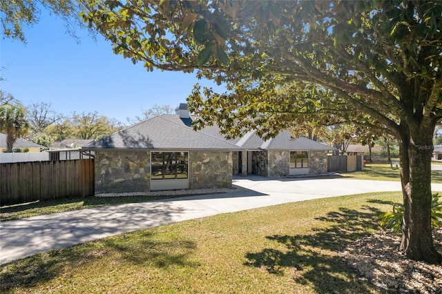 view of front of house featuring stone siding, fence, and concrete driveway