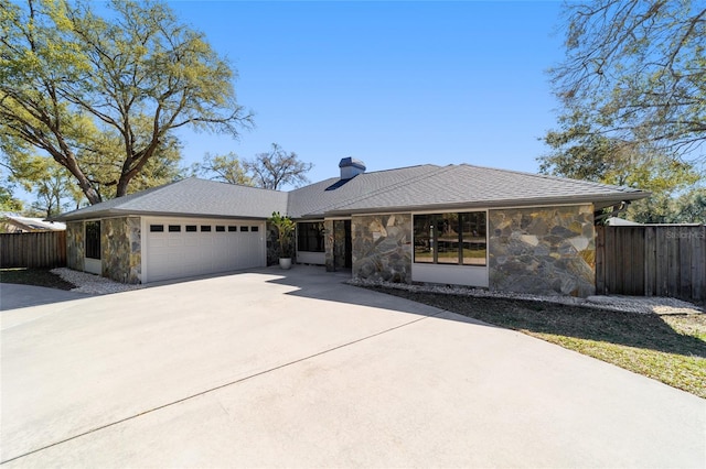 view of front of house with stone siding, driveway, an attached garage, and fence