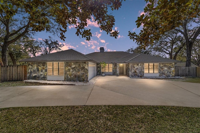 view of front of property with a garage, stone siding, fence, and driveway