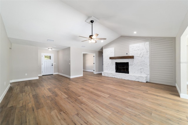 unfurnished living room with lofted ceiling, ceiling fan, a stone fireplace, and wood finished floors