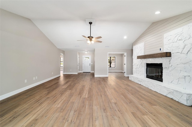 unfurnished living room featuring lofted ceiling, ceiling fan, a stone fireplace, wood finished floors, and baseboards