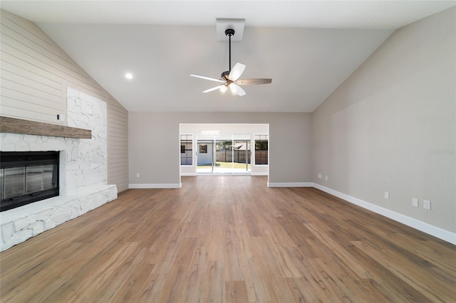 unfurnished living room with lofted ceiling, ceiling fan, a stone fireplace, wood finished floors, and baseboards