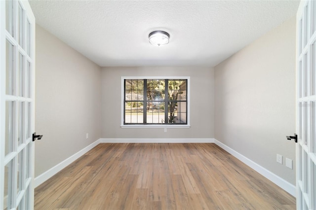 empty room with a textured ceiling, baseboards, wood finished floors, and french doors