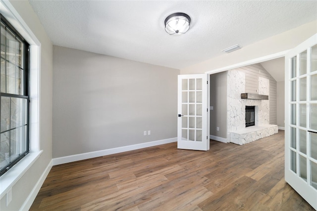 spare room with a fireplace, wood finished floors, visible vents, baseboards, and french doors