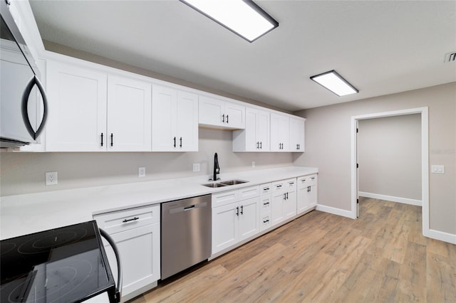 kitchen with light wood finished floors, white cabinets, a sink, black appliances, and baseboards