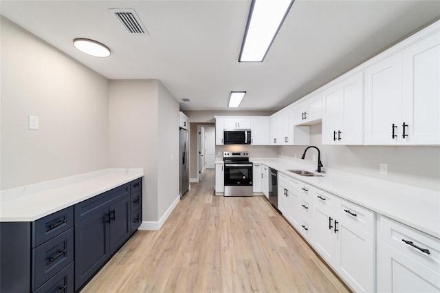 kitchen featuring light wood finished floors, stainless steel appliances, visible vents, white cabinets, and a sink