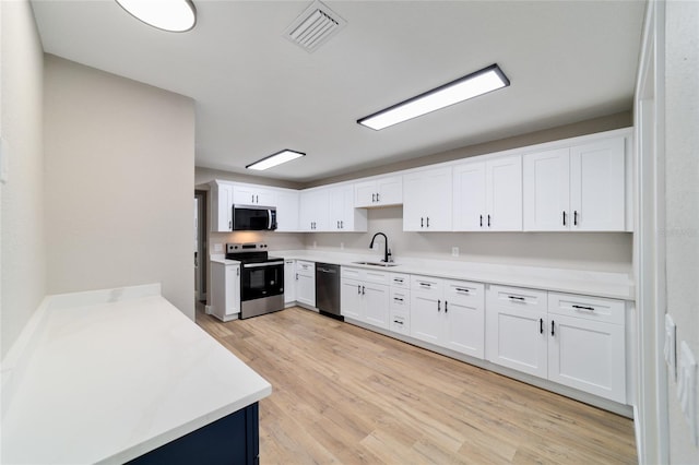 kitchen with stainless steel appliances, a sink, visible vents, white cabinetry, and light wood finished floors