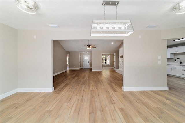 unfurnished living room with light wood-type flooring, a sink, and baseboards