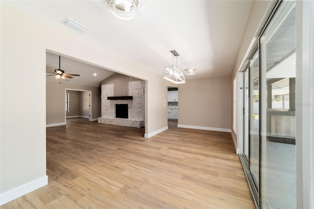 unfurnished living room with baseboards, visible vents, lofted ceiling, a stone fireplace, and light wood-style floors