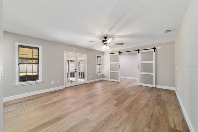 interior space featuring a textured ceiling, french doors, a barn door, and light wood-style floors