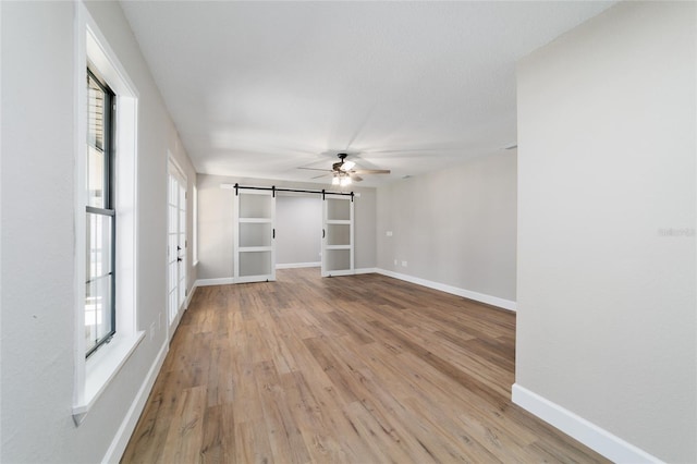 unfurnished room featuring a ceiling fan, baseboards, light wood finished floors, and a barn door