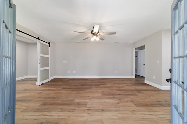 spare room featuring a ceiling fan, wood finished floors, baseboards, and a barn door