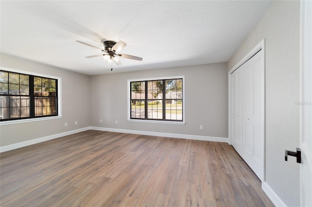 unfurnished bedroom featuring baseboards, ceiling fan, wood finished floors, a textured ceiling, and a closet