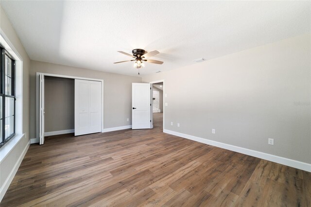 unfurnished bedroom featuring wood finished floors, visible vents, a ceiling fan, baseboards, and a closet