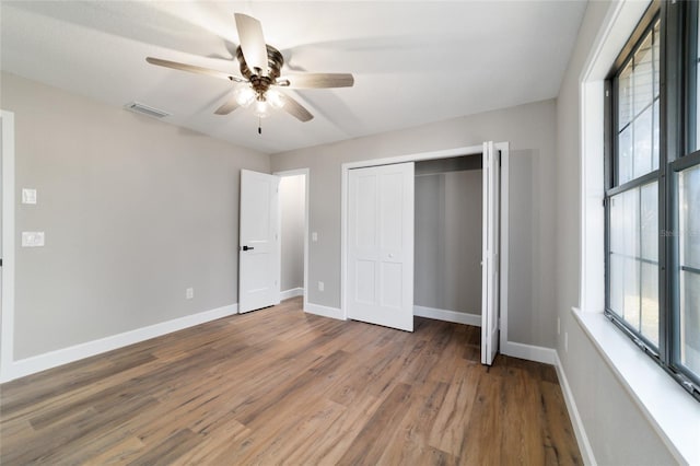 unfurnished bedroom with a closet, multiple windows, baseboards, and wood finished floors