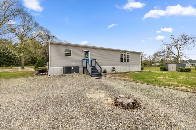 manufactured / mobile home with a storage unit, an outbuilding, driveway, a front lawn, and cooling unit