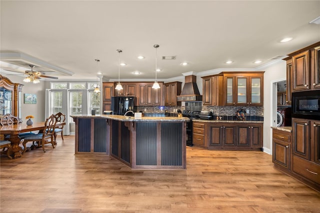 kitchen with backsplash, light wood-style floors, custom exhaust hood, and black appliances