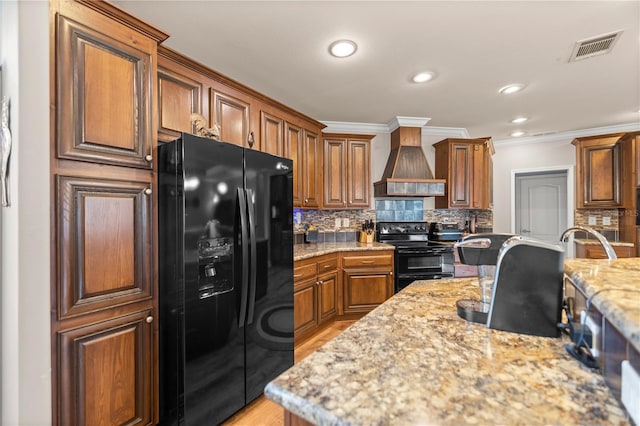 kitchen with premium range hood, visible vents, brown cabinets, black appliances, and decorative backsplash