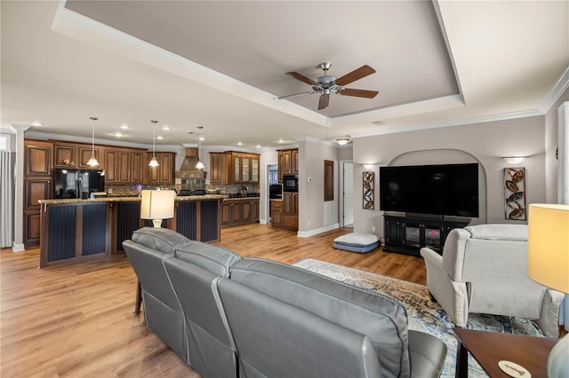 living area featuring a tray ceiling, ornamental molding, a ceiling fan, and light wood finished floors