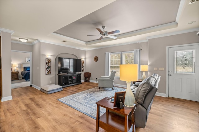 living area featuring a raised ceiling, light wood-style floors, and ceiling fan