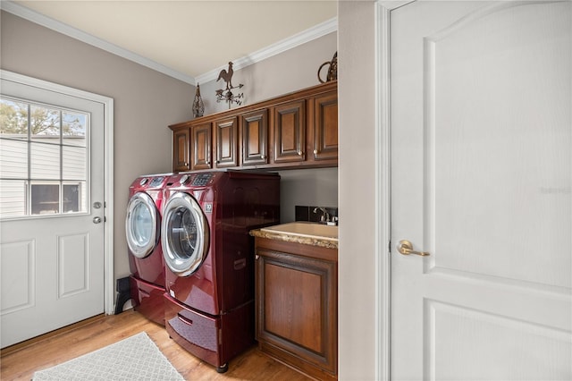 clothes washing area with cabinet space, a sink, ornamental molding, light wood-style floors, and washer and clothes dryer